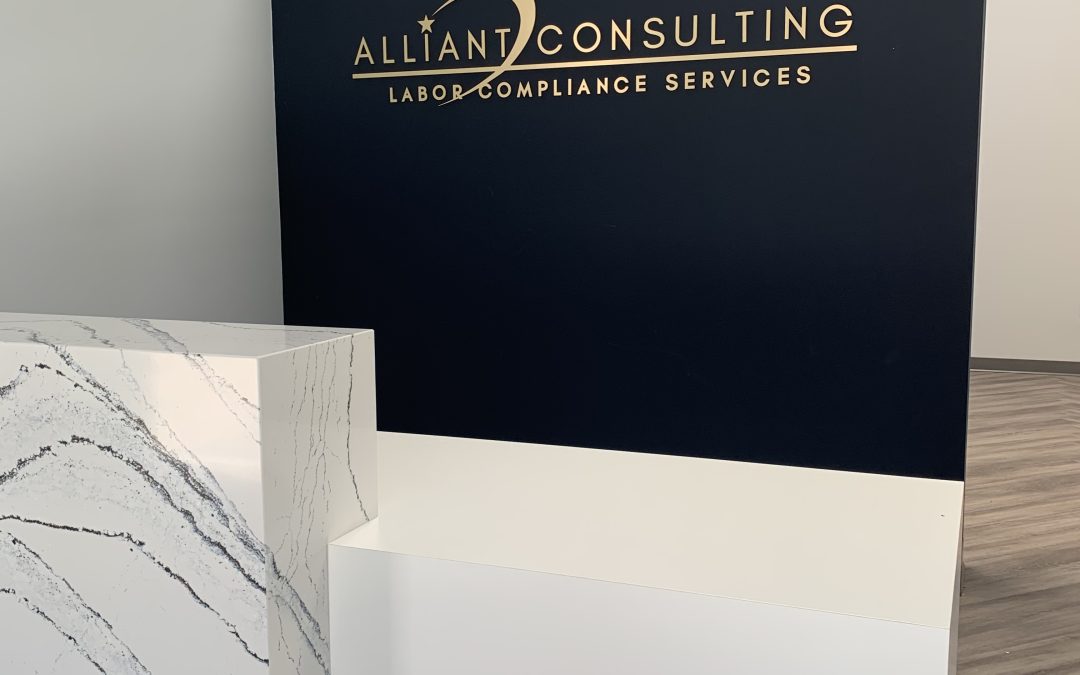 Reception area with a sign reading "Alliant Consulting Labor Compliance Services" on a dark blue wall.